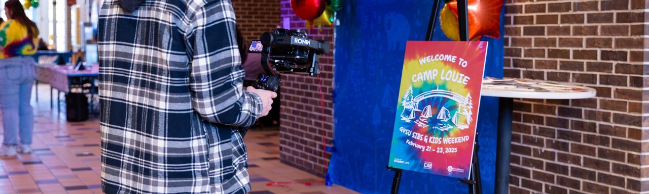 A student filming a tie dye sign that says "Welcome to Camp Louie
